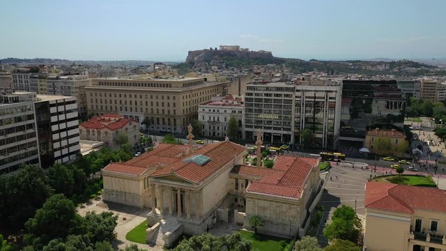 Aerial video of famous trilogy landmark buildings of Academy of Athens, Panepistimio or University, public Library with iconic Lycabettus hill at the background, Athens, Attica, Greece