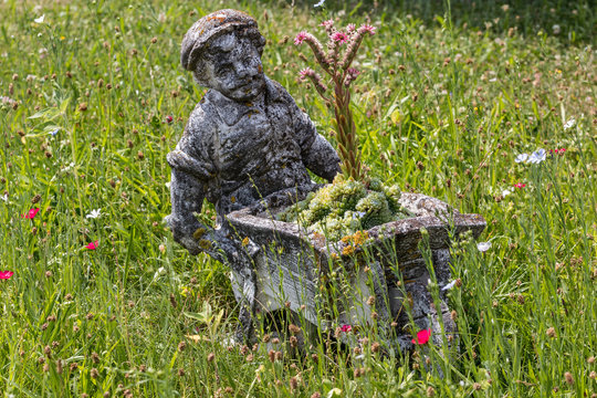 Farmer made of stone with a wheelbarrow on the middle of a wildflower meadow