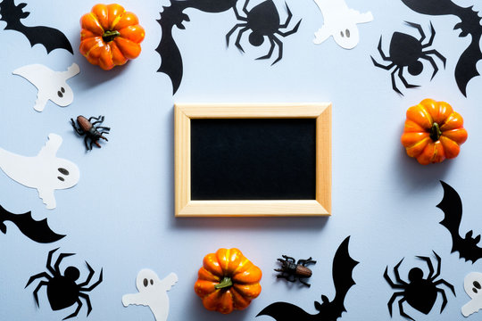 Happy halloween holiday concept. Halloween decorations, picture frame, spiders, bats, ghosts, pumpkins on blue background. Flat lay, top view, overhead.