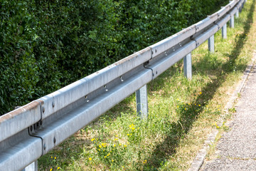 Crash barrier by the street with bushes, grass and asphalt