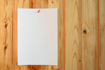 White paper sheet with red pin on natural varnished wood background. Horizontal orientation