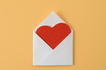 Red velvet paper heart in open white paper handmade envelope on yellow background. Valentines card. Flat lay