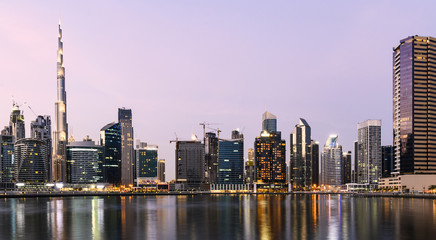 Obraz premium Oszałamiający widok na oświetloną panoramę Dubaju podczas zachodu słońca z wysokimi drapaczami chmur i kanałem wodnym płynącym na pierwszym planie. Dubaj, Zjednoczone Emiraty Arabskie.