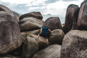 Athletic fit male traveller climbs rocks on a hike in Florianopolis, Brazil