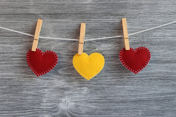 Valentine day background. Red and yellow felt handmade hearts hanging on a white string with wooden clothes pins against a gray wooden surface