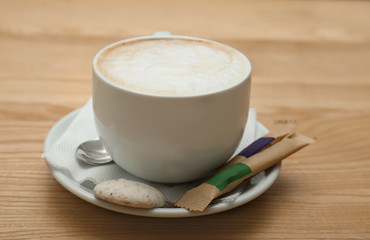 Cup of aromatic cacao with sugar sticks and cookie on wooden table