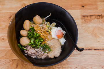 Delicious spicy noodles put on a black cup on a wooden table