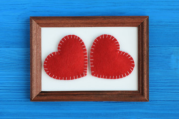 Two cute red felt handmade hearts lying on a brown frame on a blue wooden background. Top view. Flat lay