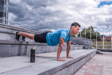 male athlete, man summer city, push-ups, lying on bench, chest training, press bar, bottle protein with water, fitness workout morning, background concrete steps. Free space for motivation text.
