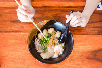 The woman hand is going to eat a delicious spicy noodles in a black cup placed on a wooden table.