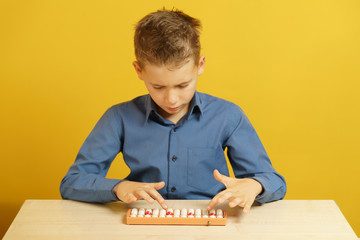 The boy in the blue shirt sitting at the table and thinks on the soroban. Mental arithmetic