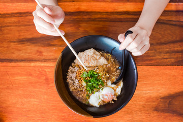 The woman hand is going to eat a delicious spicy noodles in a black cup placed on a wooden table.