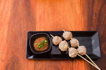 Grilled meatballs placed on a black plate with dipping sauce on wood background