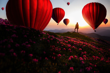 Hiker woman standing with hands up achieving the top. Colorful hot air balloons flying over mountain. Girl welcomes a sun