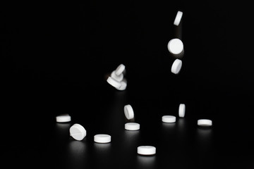 White pills falling on black background. Copy space. Tablets in the air