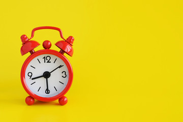 Cute red metal alarm clock on yellow background. Half past eight. Copy space