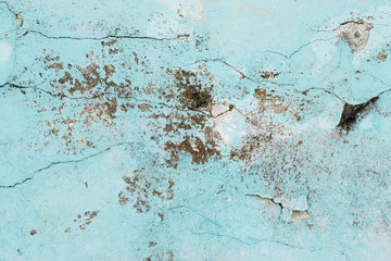Weathered concrete wall with stains, cracks, blue peeling paint and some moss