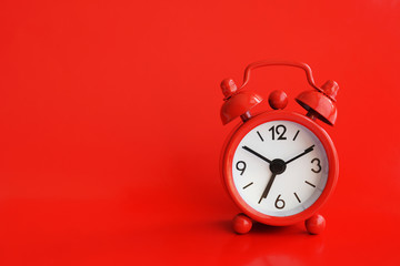 Cute red metal alarm clock on red background. Ten to seven. Copy space