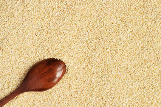 Brown wooden spoon placed inverted on natural white sesame seeds. Top view