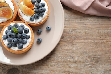 Tarts with blueberries and figs served on wooden table, top view with space for text. Delicious pastries