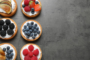 Tarts with different berries on grey table, top view with space for text. Delicious pastries