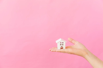 Simply design female woman hand holding miniature white toy house isolated on pink pastel colorful...