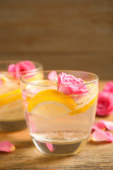 Tasty refreshing lemon drink with roses on wooden table