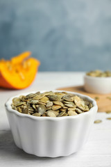 Bowl of raw pumpkin seeds on white wooden table against blue background. Space for text