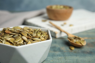 Bowl of raw pumpkin seeds on blue wooden table, closeup. Space for text