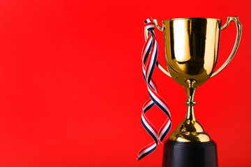 Golden trophy cup with ribbon on red background. Space for text
