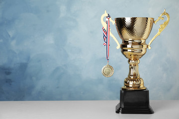 Golden trophy cup and medal on table against blue background. Space for text