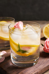 Delicious refreshing drink with lemon and roses on wooden table