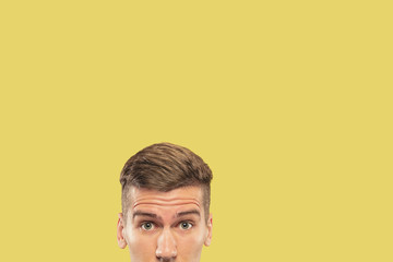 Caucasian young man's close up shot on yellow studio background. Beautiful male model with well-kept skin. Concept of human emotions, facial expression, sales, ad. Looking at camera wondered