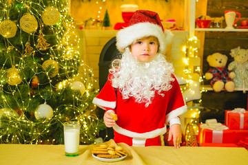 Fototapeta na wymiar Cookies for kids Santa Claus. Portrait of little Santa child holding chocolate cookie and glass of milk. Santa kids picking cookie. Little Santa picking cookie and glass of milk at home.