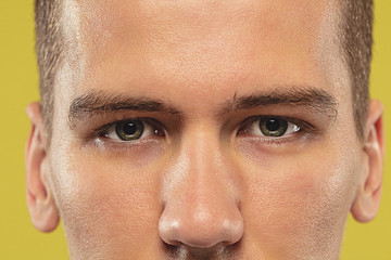 Obraz premium Caucasian young man's close up on yellow studio background. Beautiful male model with well-kept skin. Concept of human emotions, facial expression, sales, ad. Copyspace. Eyes looking at camera.