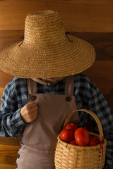 the woman wearing county style clothes and wicker hat stands in front of wooden wall.