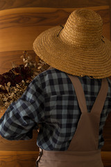 the woman wearing county style clothes and wicker hat stands in front of wooden wall.