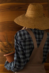 the woman wearing county style clothes and wicker hat stands in front of wooden wall.