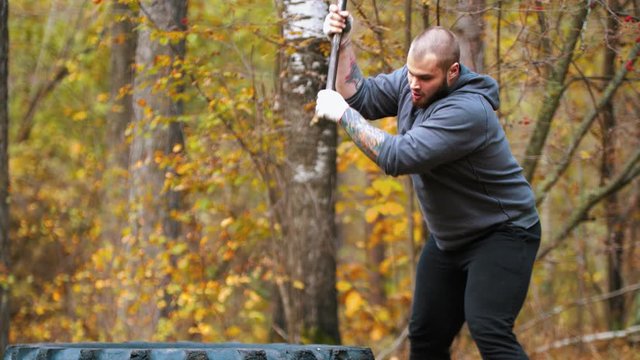 A big man bodybuilder hitting the truck tire with a metal hammer - autumn forest