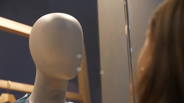 A girl looks through a window on a mannequin