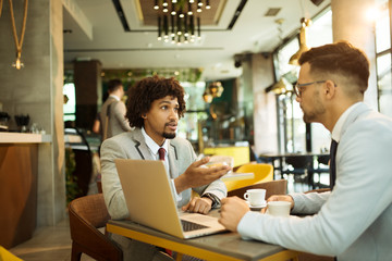 Obraz premium Young businessmen sitting at a coffee shop and talking about business
