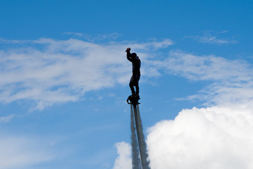a man on a flyboard rose against the clouds, water show in the city, doing somersaults, water splashes, contour and Siluet lighting.