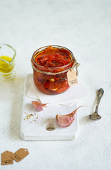 Sun-dried tomato with oil and garlic in the glass on wood board and the white background. Copy space.