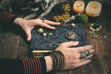 Sorceress woman is reading ancient magic book in the light of candles.