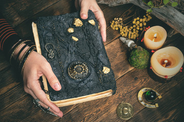 Sorceress woman is reading ancient magic book in the light of candles.