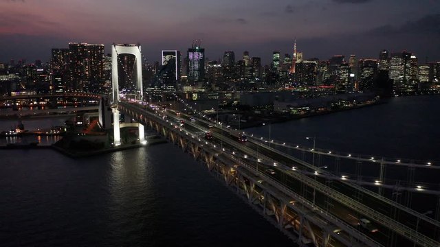 alt dusk flying backward alongside Rainbow Bridge in Tokyo