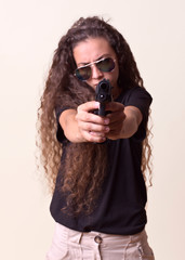 Young long curly hair girl with sunglasses and a gun in her hand poses would be in front of a colored background