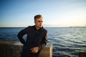 Confident and handsome young man standing near river. Street style clothes.