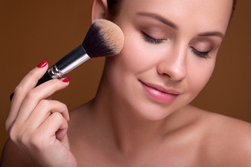 Caucasian brunette woman apply blush on a cheekbone with a brush. Close up portarait. Skin care ...