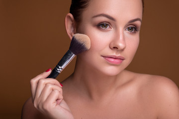 Caucasian brunette woman apply blush on a cheekbone with a brush. Close up portarait. Skin care  concept